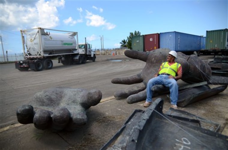 In this picture taken Sept. 2, 2011, Jose Rivera, a worker of the port of Mayaguez, rests on a giant hand, one of many pieces of a Christopher Columbus statue strewn across the port storage area in Mayaguez, Puerto Rico. The Columbus statue would be the tallest structure in the Caribbean and among the tallest statues in the world, a monument in a region where Columbus has not been regarded highly for many years. (AP Photo/Olimpo Ramos) PUERTO RICO OUT - NO PUBLICAR EN PUERTO RICO